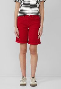Shorts en denim rouge avec un ourlet roulé, design à cinq poches et fermeture à bouton en métal, associés à un t-shirt rayé noir et blanc et des baskets.
