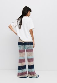 Witte oversized t-shirt gecombineerd met meerkleurige gestreepte gehaakte flared pants met een mix van blauwe, paarse en beige tinten.