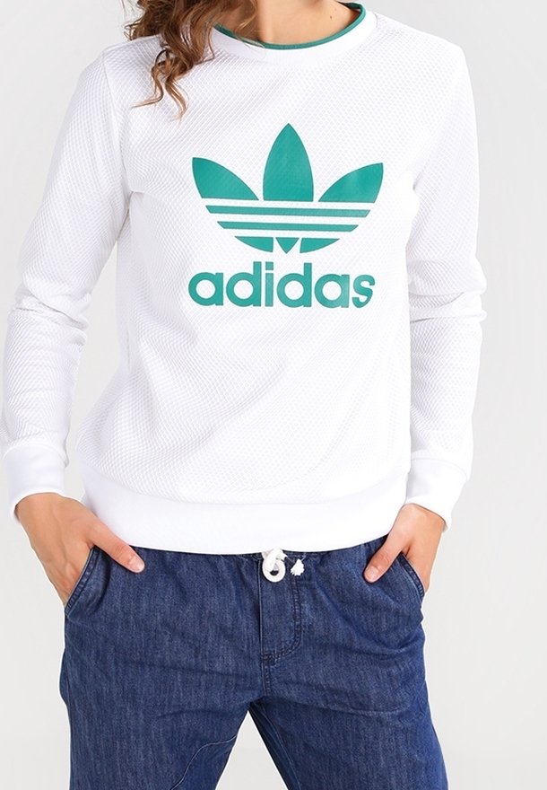 Sweat-shirt Adidas blanc avec texture en maille, logo trèfle vert, poignets et col côtelés. Assorti avec un pantalon bleu à cordon de serrage.