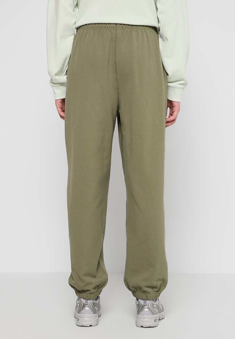 Pantalons de survêtement vert olive avec une taille élastique et des chevilles resserrées, en tissu doux et texturé. Portés avec des baskets argentées.