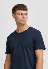 Sötétkék pamut póló rövid ujjakkal, kerek nyakkivágással és sima textúrával, egy oldalra néző modellen viselve.