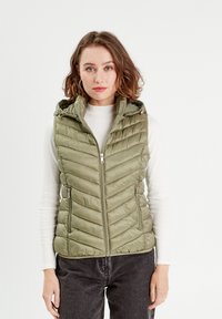 Gilet matelassé vert olive avec capuche, présentant une fermeture éclair à l'avant, un motif en chevrons et deux poches latérales zippées.