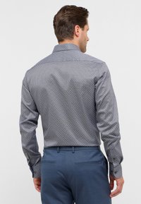 Gestreepte overhemden in marineblauw, met een geometrisch ontwerp. Lange mouwen, gestructureerde kraag en een getailleerde pasvorm, gecombineerd met blauwe broeken.