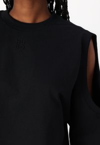 Sudadera negra con cuello acanalado y detalles de hombro cortados. Presenta el logotipo embosado "HUGO" en el frente. Textura suave, ajuste casual.
