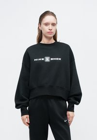 Černá zkrácená mikina s kulatým výstřihem, na přední straně s bílým logem "NIKE SHOX". Spárovaná s černými tepláky.