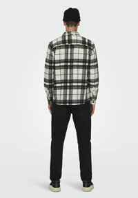 Camisa de franela a cuadros en blanco y negro con botones, mangas largas y cuello, combinada con jeans negros y zapatillas negras con acentos morados.