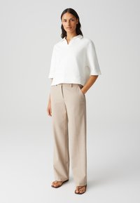 Witte polo met kort mouw en kraag, gecombineerd met beige wijde broek. De outfit heeft een relaxed fit en is gemaakt van zachte materialen.