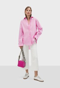 Rosa Hemd mit Kragen, weiße weit geschnittene Hose und weiße Sneakers mit braunen Sohlen. Eine kleine rosa Tasche mit einem gemusterten Riemen ist ebenfalls enthalten.