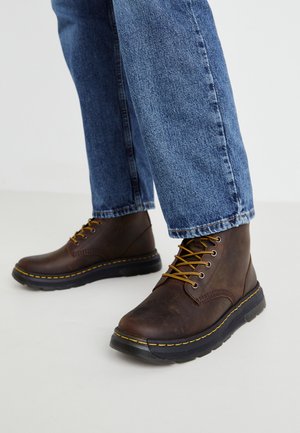 Pruunist nahast pahkluu saapad kollaste paeltega, ümar varvas ja must kummitald. Kanda koos siniste teksadega, esitades juhusliku välimuse.