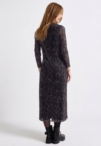 Długa, dopasowana sukienka z przezroczystej, teksturowanej tkaniny w czarno-brązowy wzór w cętki. Posiada długie rękawy i prosty dół.