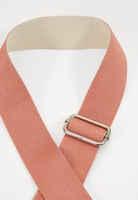 Tirantes de algodón en un tono coral con una superficie texturizada, que presentan una hebilla de metal y una capa interior beige en contraste.