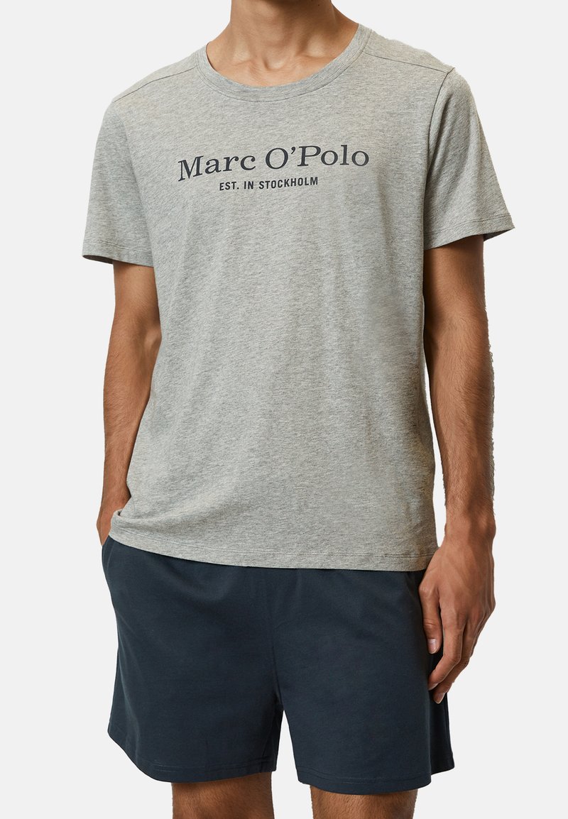 Šedé bavlnené tričko s krátkymi rukávmi, ktoré má tmavý potlač loga "Marc O'Polo EST. IN STOCKHOLM" na hrudi. Strih je voľného strihu.