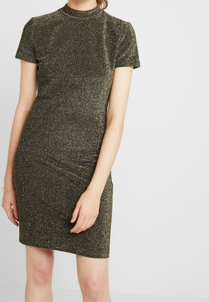 Femme portant une robe ajustée à manches courtes, longueur genou, noire et dorée pailletée, sur un fond clair uni.