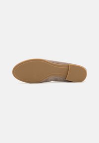 Zapato de ante beige con suela de goma. El diseño presenta una punta redondeada y una textura suave, con un tacón plano para mayor estabilidad.