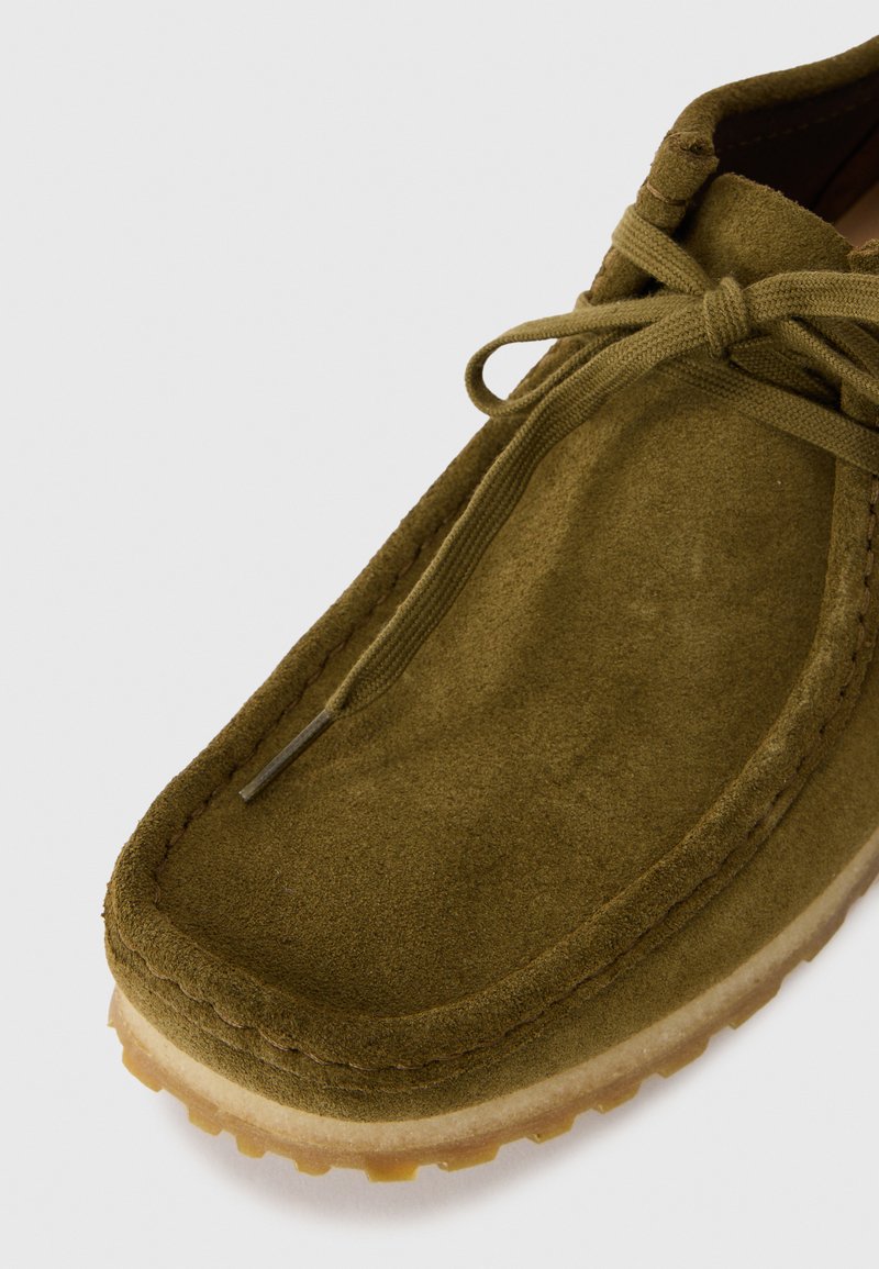 Zapato de ante verde con puntera redondeada, diseño de cordones y suela de goma texturizada con pequeñas protuberancias para mayor tracción.