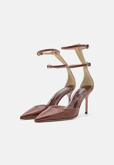 Zapatos de tacón alto de charol marrón con diseño de punta afilada, correas ajustables en el tobillo y tacones de aguja. Textura suave y acabado brillante.
