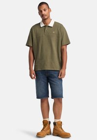 Olivgrön polotröja med vit krage, i kombination med denimshorts. Bärs med bruna stövlar med gula snören och krämfärgade strumpor.