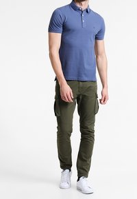 Polokošile z lehkého modrého bavlněného materiálu s trojicí knoflíků, spárovaná s olivovými cargo kalhotami. Bílé tenisky dokončují celý outfit.