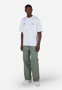 Biała bawełniana koszulka z haftowanym brązowym napisem. Połączona z luźnymi jasnoniebieskimi dżinsami z bocznymi paskami w burgundowym i białym kolorze.