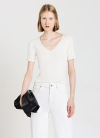 Top bianco a coste con maniche corte e scollo a V, abbinato a jeans bianchi a vita alta e una borsa a tracolla nera.