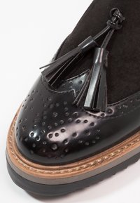 Černá kožená bota s hladkým, perforovaným povrchem, akcentem z semiše a dekoračními třásněmi. Obsahuje silnou podrážku a detailní švy.