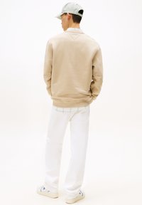 Sudadera beige con tejido texturizado, pantalones blancos y gorra verde clara. La parte trasera muestra un diseño simple y limpio con costuras notables.