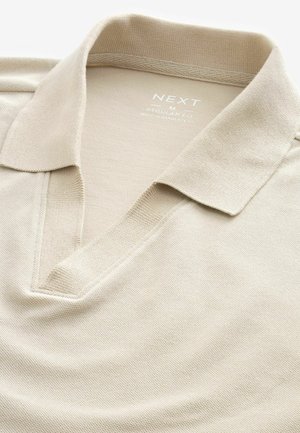 Polo beige realizzato in tessuto testurizzato, con scollo a V e colletto aperto. L'etichetta riporta "NEXT M REGULAR FIT."