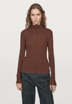 Brown, long-sleeve turtleneck top made of soft material with a straight fit and subtle seam detail down the center. Paired with dark denim pants.