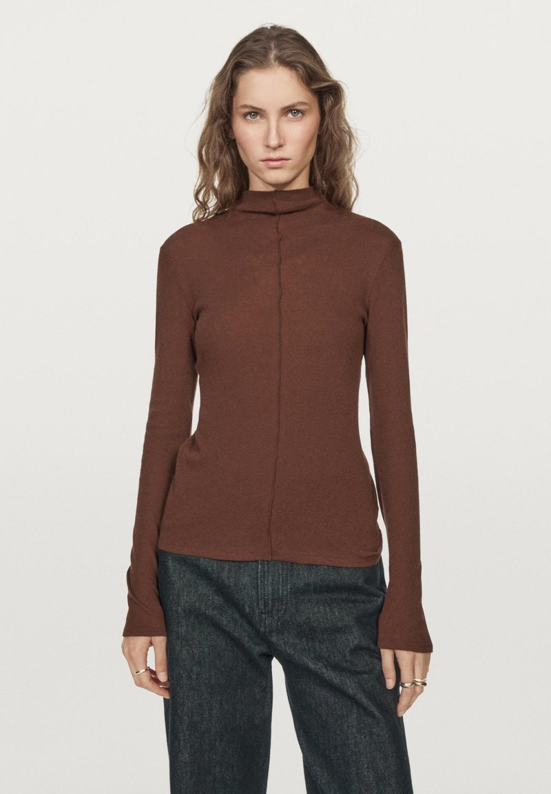Bruine, lange mouwen turtleneck top gemaakt van zacht materiaal met een rechte pasvorm en subtiele naaddetail in het midden. Gecombineerd met een donkere spijkerbroek.