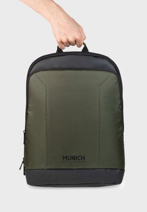 Grüner Rucksack aus Stoff mit strukturierter Oberfläche, schwarzen Akzenten und einem Tragegriff oben. Verfügt über ein Reißverschlussfach und ein Logo am unteren Rand.