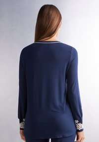 Marineblauw langemouwenblouse gemaakt van zachte stof, met delicate kantafwerking aan de mouwen en een simpele ronde halslijn.