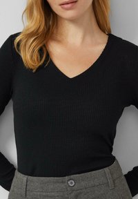 Czarny prążkowany sweter z dekoltem w serek i długimi rękawami, wykonany z fakturowanej tkaniny. Połączony z szarymi spodniami, ozdobionymi detalem z guzikiem.