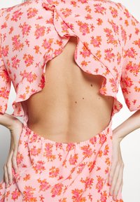 Rosa blommig klänning med volangärmar och låg rygg, elastisk midja, prydd med små mönster av orangea och rosa rosor.