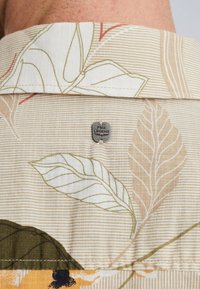 Kortærmet skjorte i beige med stribet mønster, prydet med blomster grafik i grøn, gul og sort, samt et metal logo tag ved kraven.