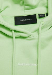 Felpa verde chiaro con cordino, texture morbida e un'etichetta con logo. Presenta un'etichetta di taglia 'S' e un'etichetta 'Made in Turkey'.