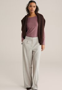 Brūns adīts veste pār rozā garām piedurknēm topu, saskaņota ar gaiši pelēkām platām biksēm ar priekšējiem krokām. Vienkārši rotaslietu akcenti.