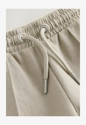 Pantalones deportivos beige con cintura elástica con ojales plateados y cordones beige. Tejido de mezcla de algodón suave con textura lisa.