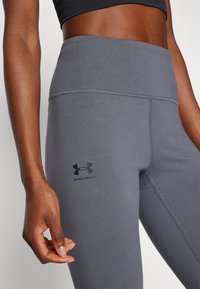 Grå treningsleggings med høy livlinje, sømløst design og et Under Armour-logo på låret. Glatt, elastisk tekstur.