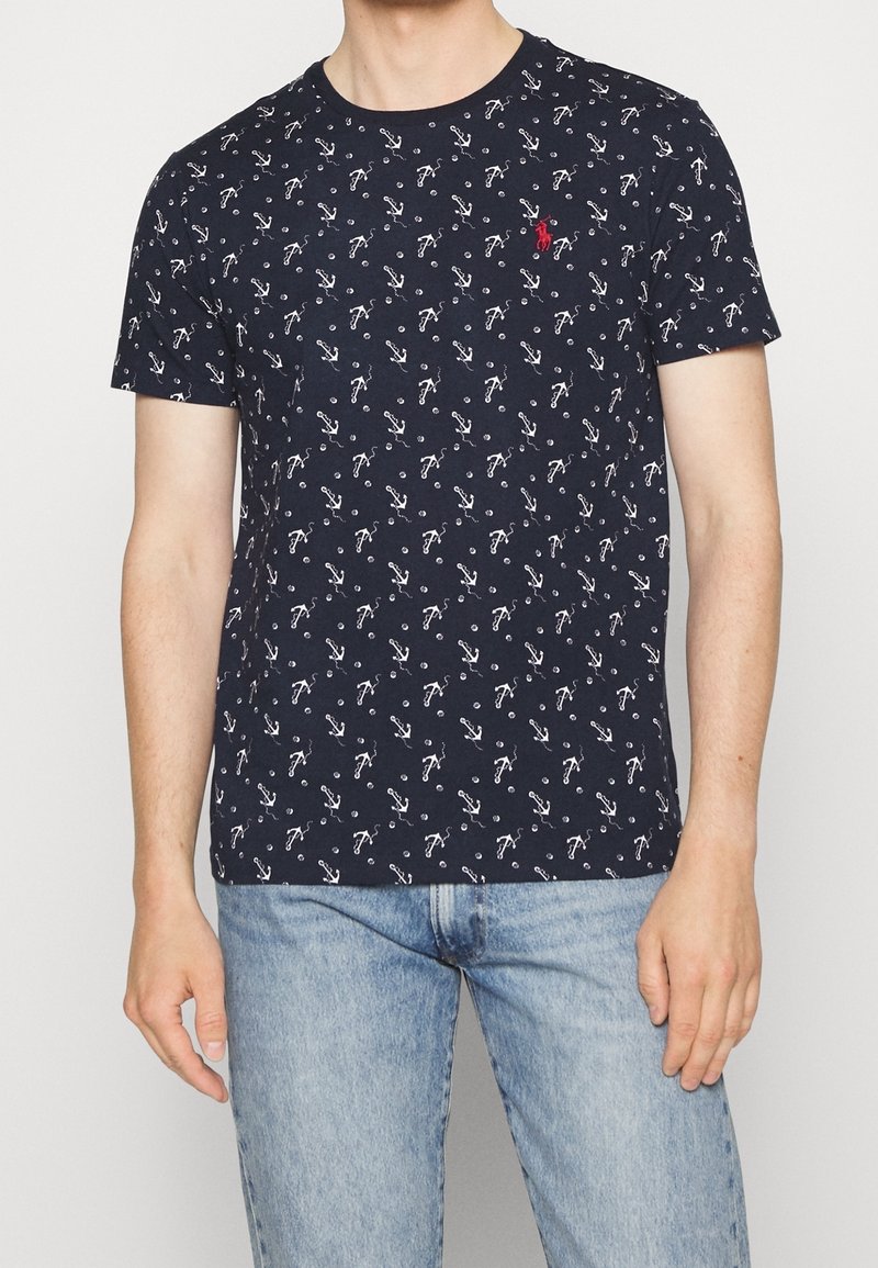 Navy t-shirt featuring a repeated white anchor pattern, crew neckline, short sleeves, and a small red logo on the chest.