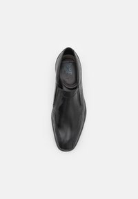 Zapato negro de piel tipo slip-on con un acabado suave, forma alargada y detalles de costura sutiles. Interior forrado con la marca 'bugatti' visible.