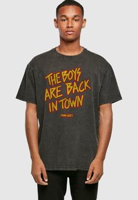 Sort oversized t-shirt i bomuld, med rød og gul grafisk tekst "THE BOYS ARE BACK IN TOWN" fra "THIN LIZZY." Slidt finish.
