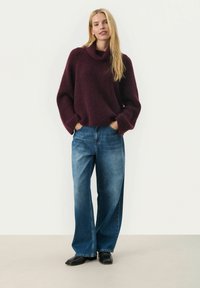 Bordeaux gebreide trui met een col, gecombineerd met lichtblauwe wijde jeans. De trui heeft een gestructureerde afwerking en de jeans hebben een strakke lijn.
