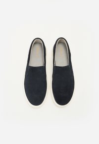Scarpe slip-on in suede blu navy con suole in gomma bianche, design a punta rotonda e fodera interna testurizzata. Stile minimalista senza hardware visibile.
