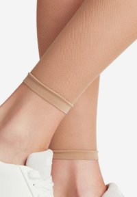 Beige visnetleggingen met een textuurpatroon, voorzien van een gladde, effen tailleband; gecombineerd met een witte sneaker bij de enkels.