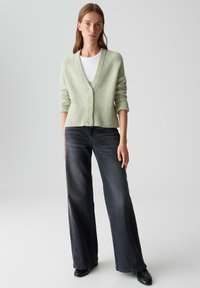 Lichtgroene wolblend cardigan met een diepe V-hals, geribde zoom en vijf ronde knopen, gecombineerd met wijde donkere denim jeans.