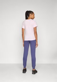 T-shirt rose clair à manches courtes associé à un pantalon de survêtement violet, avec des poignets élastiques et une coupe décontractée, porté avec des chaussures de sport noires.