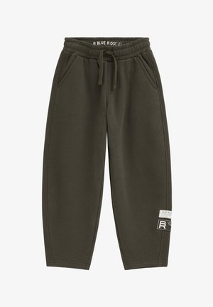 Jogginghose aus olivgrünem Fleece mit elastischem Bund, Kordelzug, Seitentaschen und zwei Stoffflicken am unteren rechten Bein.