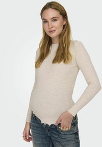 Lichtbeige geribbelde longsleeve met een ronde halslijn, met een licht gebogen zoom en een gestructureerde stof. Draagt samen met versleten blauwe spijkerbroek.