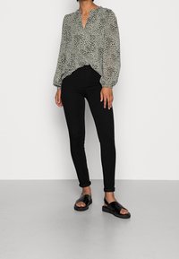 Ljusgrön, genomskinlig blus med lång ärm och V-hals, prydd med svart prickmönster; tillsammans med svarta skinny jeans och svarta slidesandal.