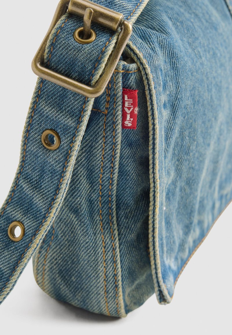 Borsa a tracolla in denim blu con tracolla regolabile, fibbia in ottone, cuciture arancioni e etichetta rossa Levi's sul lato.